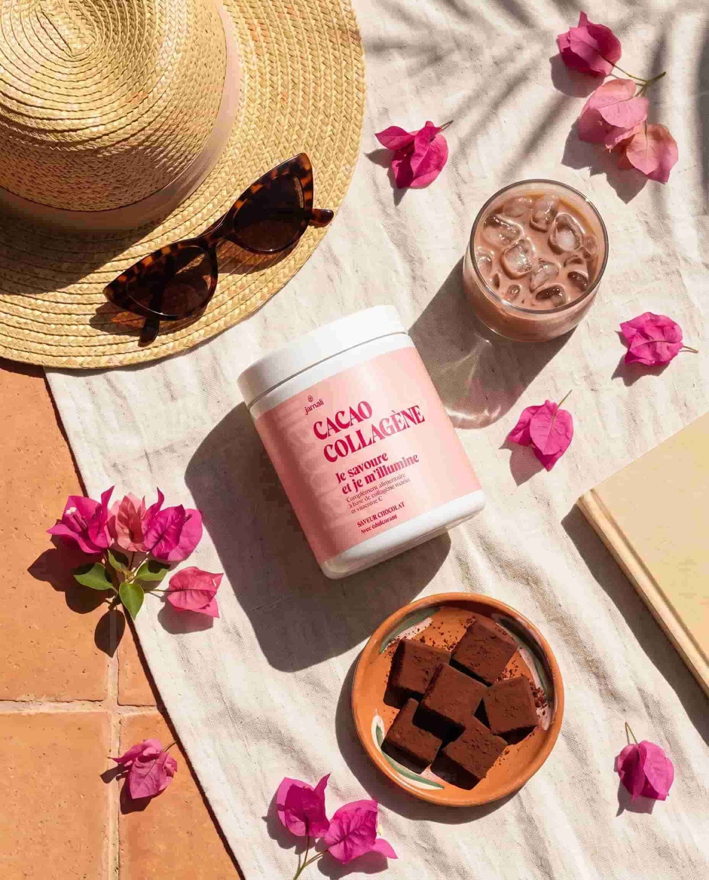 Flatlay estival avec le pot de Cacao Collagène Jamali, chapeau de paille, boisson glacée et fleurs de bougainvillier