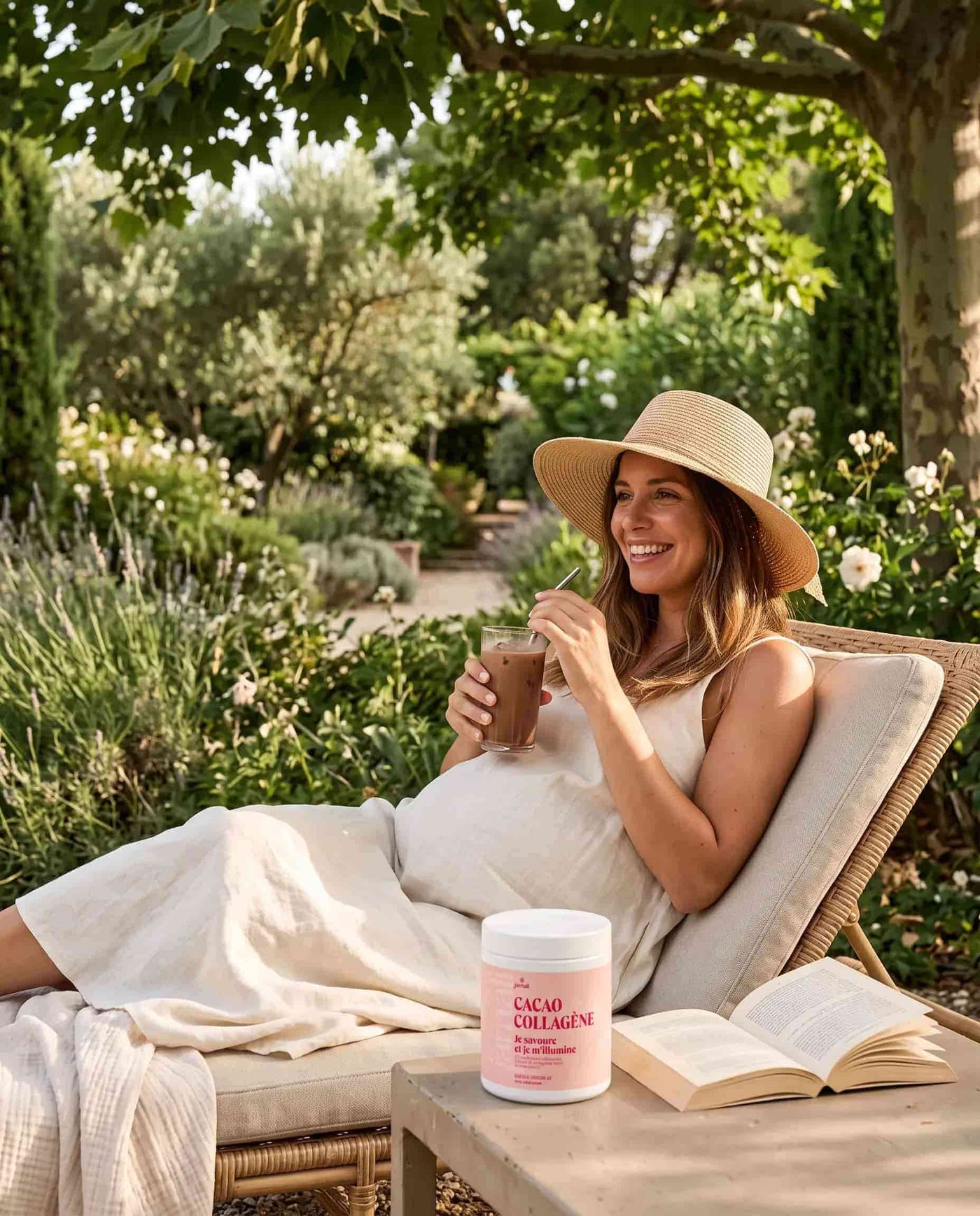 Femme enceinte au chapeau de paille dégustant sa boisson Cacao Collagène dans un jardin méditerranéen
