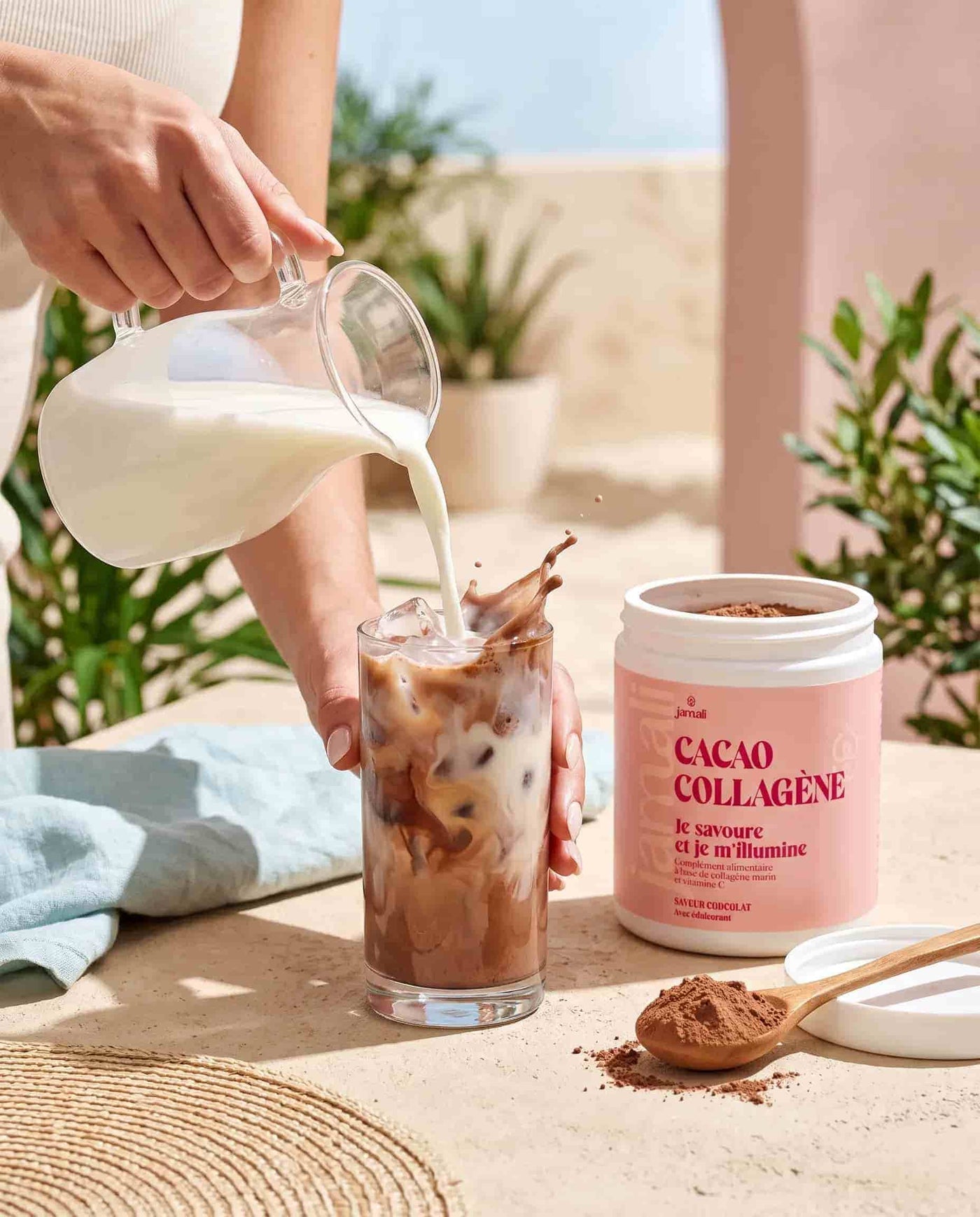 Versement de lait dans un verre de Cacao Collagène Jamali glacé, cuillère de poudre à côté